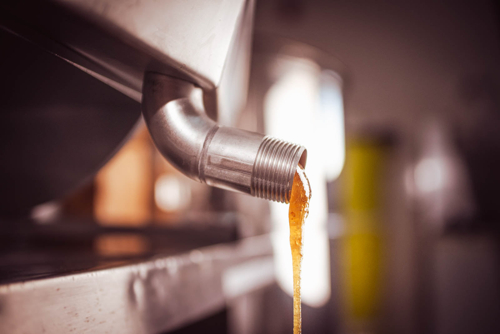 Aus einem Edelstahlauslaufhahn in Nahaufnahme tropft dunkler, nicht gesiebter Presshonig