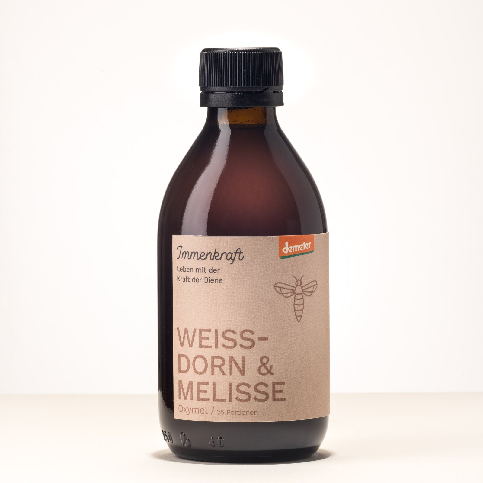 Eine Braunglas-Flasche mit der Aufschrift Immenkraft - Leben mit der Kraft der Biene, Demeter-Logo und Bienen-Logo. Produktname: Weissdorn & Melisse Oxymel, 25 Portionen.