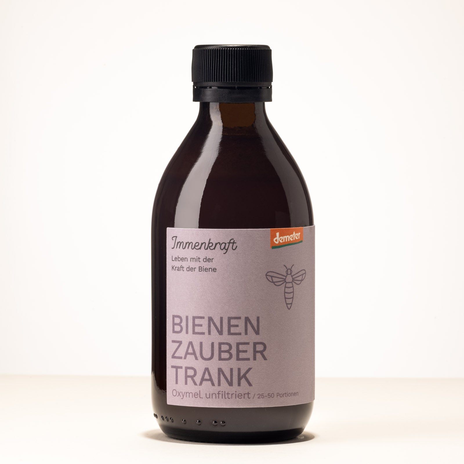 Eine Braunglas-Flasche mit der Aufschrift Immenkraft - Leben mit der Kraft der Biene, Demeter-Logo und Bienen-Logo. Produktname: Bienenzaubertrank Oxymel, unfiltriert, 25-50 Portionen.