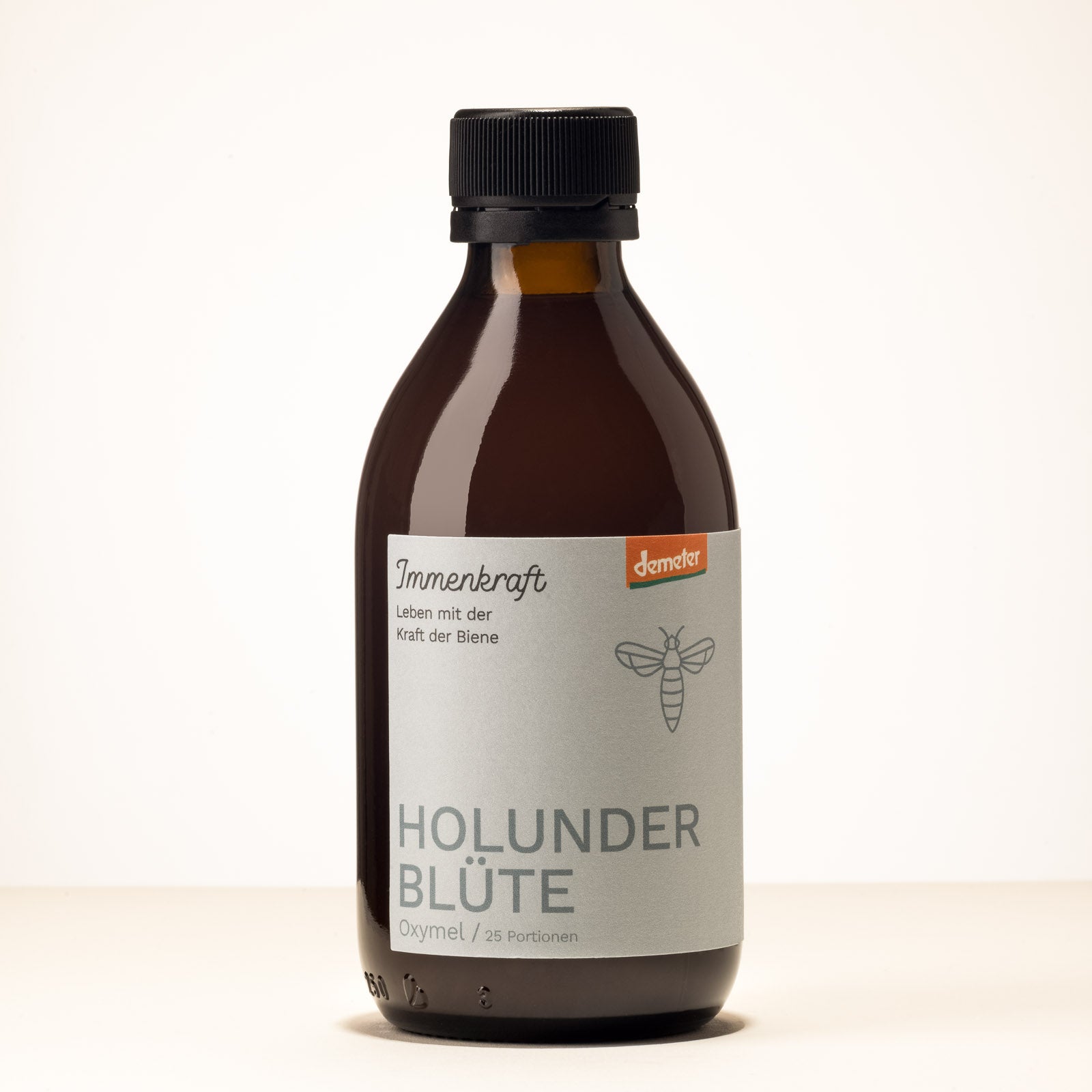 Eine Braunglas-Flasche mit der Aufschrift Immenkraft - Leben mit der Kraft der Biene, Demeter-Logo und Bienen-Logo. Produktname: Holunderblüte Oxymel, 25 Portionen.